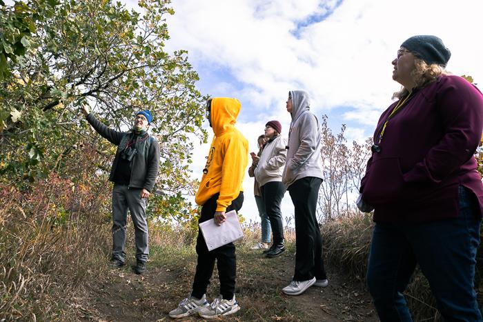 Jason St. Saveur (far right), senior education manager for Spring Creek Prairie Audubon Center, points toward a tree along one of the center's trails. Three Doane University students and librarian Cali Biaggi listen. 