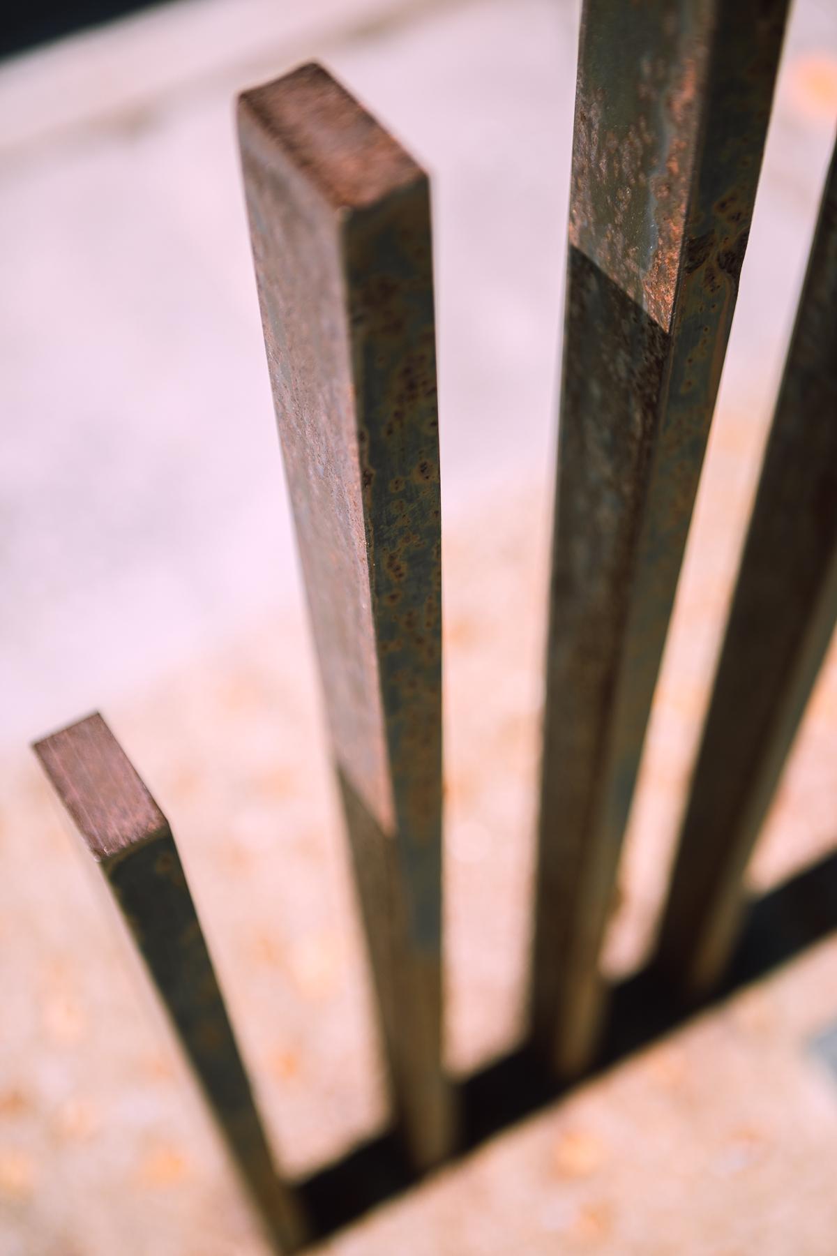 What looks like four rectangular metal posts rise out of a yellow-lichen covered concrete base. 它们的一边有厚厚的阴影. 