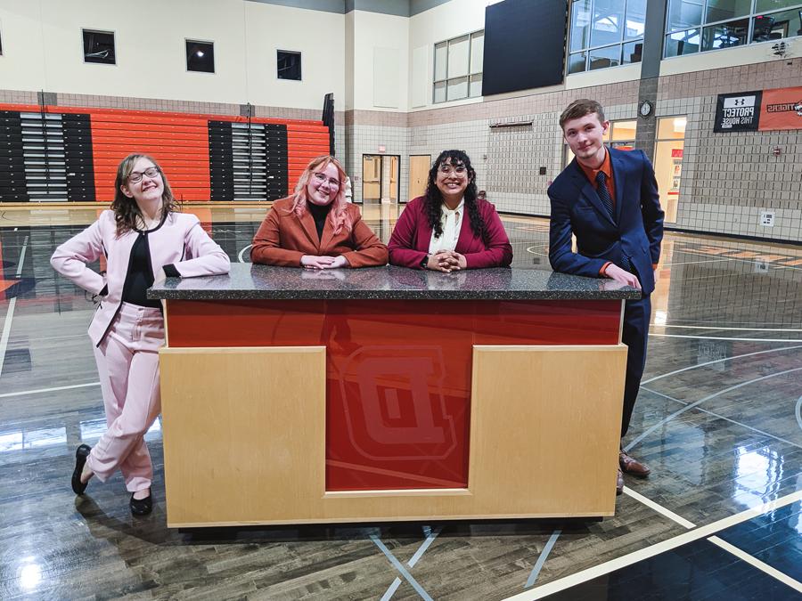 Four of Doane's five forensics team members pose at a desk in their suits during a tournament held on the university's Crete campus. 