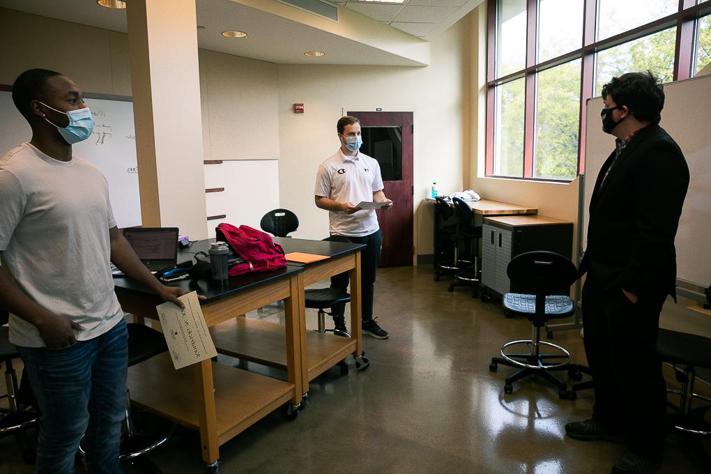 Dr. 凯尔Stolle presents scholarships to senior engineering students Ryan Lasauskas, 左, and Kenny Kemp, 正确的. They are standing in a classroom in the Lied Science and Mathematics building.