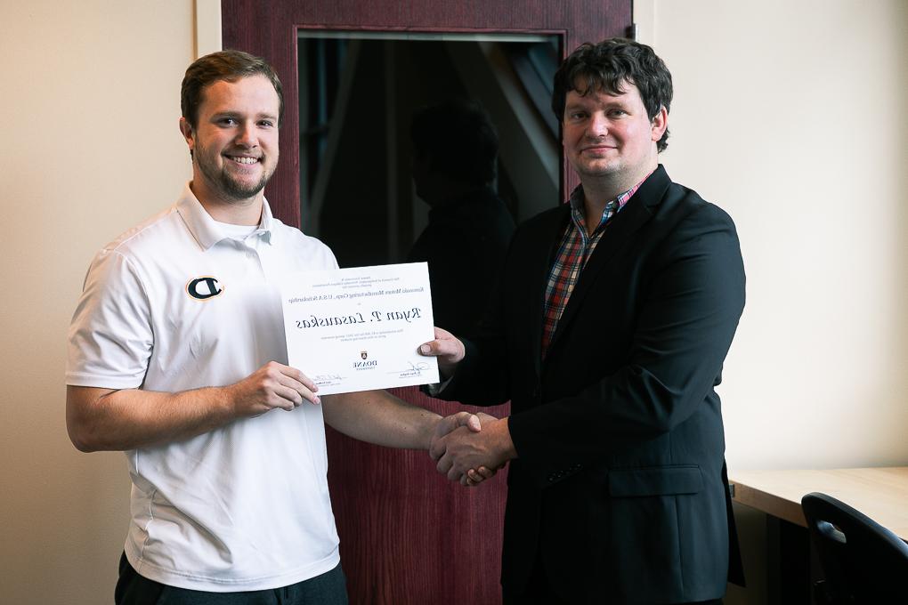 Senior engineering student Ryan Lasauskas holds up his scholarship while standing next to Dr. 凯尔Stolle.