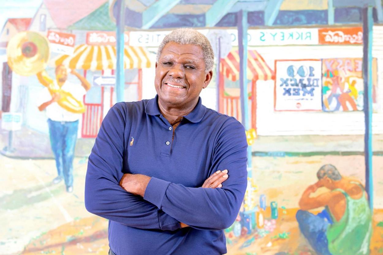 Artist Gilbert Fletcher stands in front of one of his paintings.